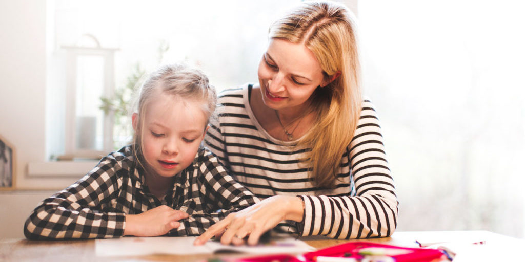 A little girl doing a written task with her mother at a table